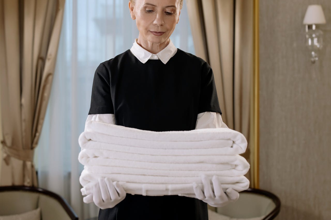 Professional housekeeper holding a stack of fresh towels in a luxurious hotel room, showcasing elegance and service.